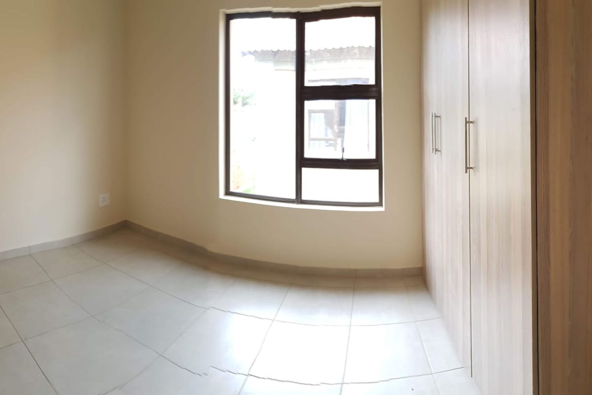 A bright, empty bedroom featuring neutral tiled flooring and built-in wooden cabinetry, offering a clean and versatile space.