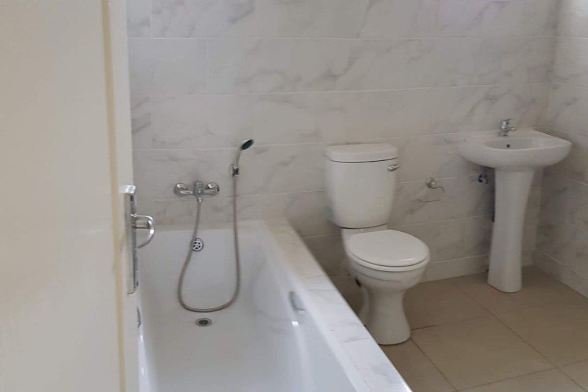 A clean, functional bathroom featuring a built-in bathtub with shower attachment, a pedestal sink, and a standard toilet, finished with light-toned wall tiles.