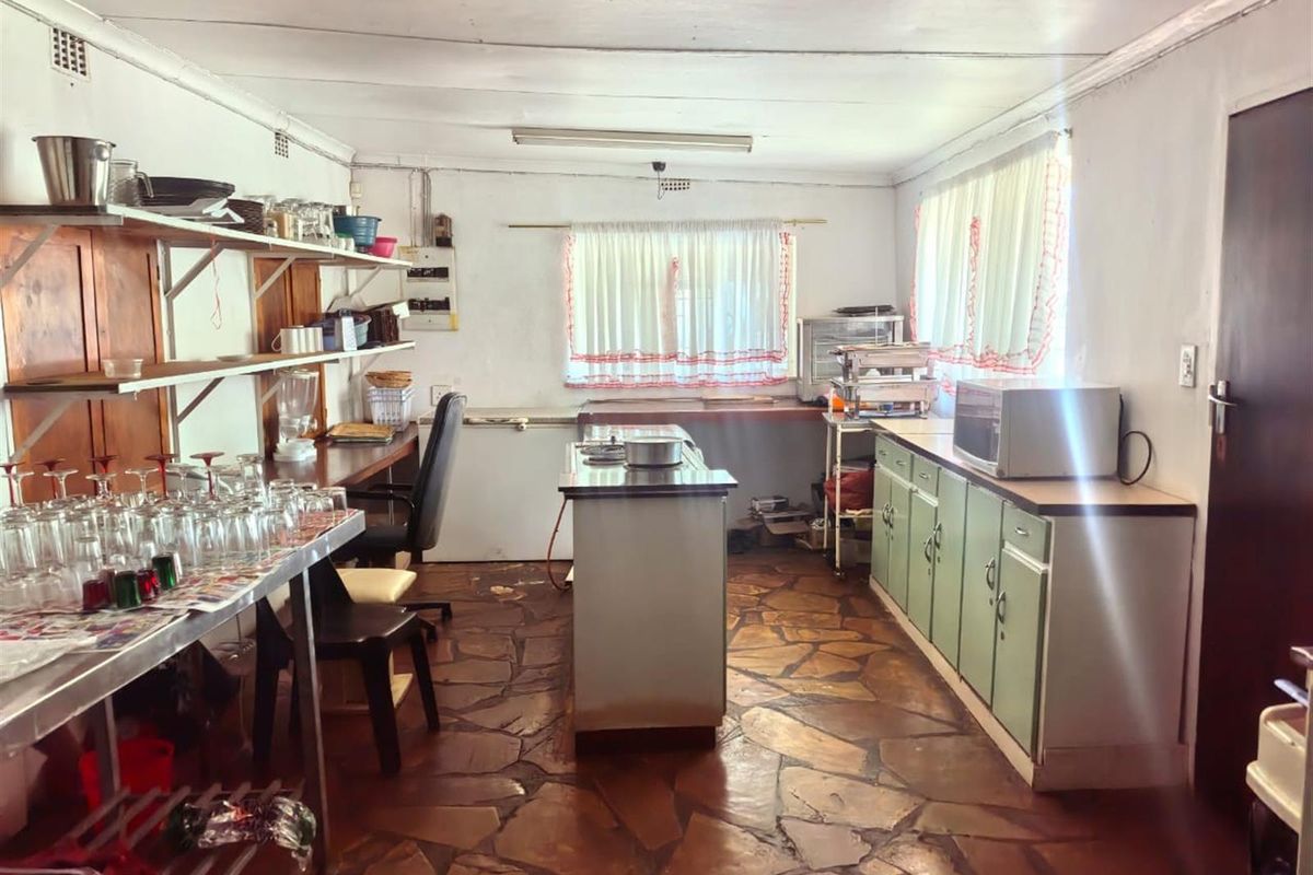 A functional kitchen area featuring stone flooring, built-in cabinetry, and fixed shelving, offering potential for modernization and layout optimization.