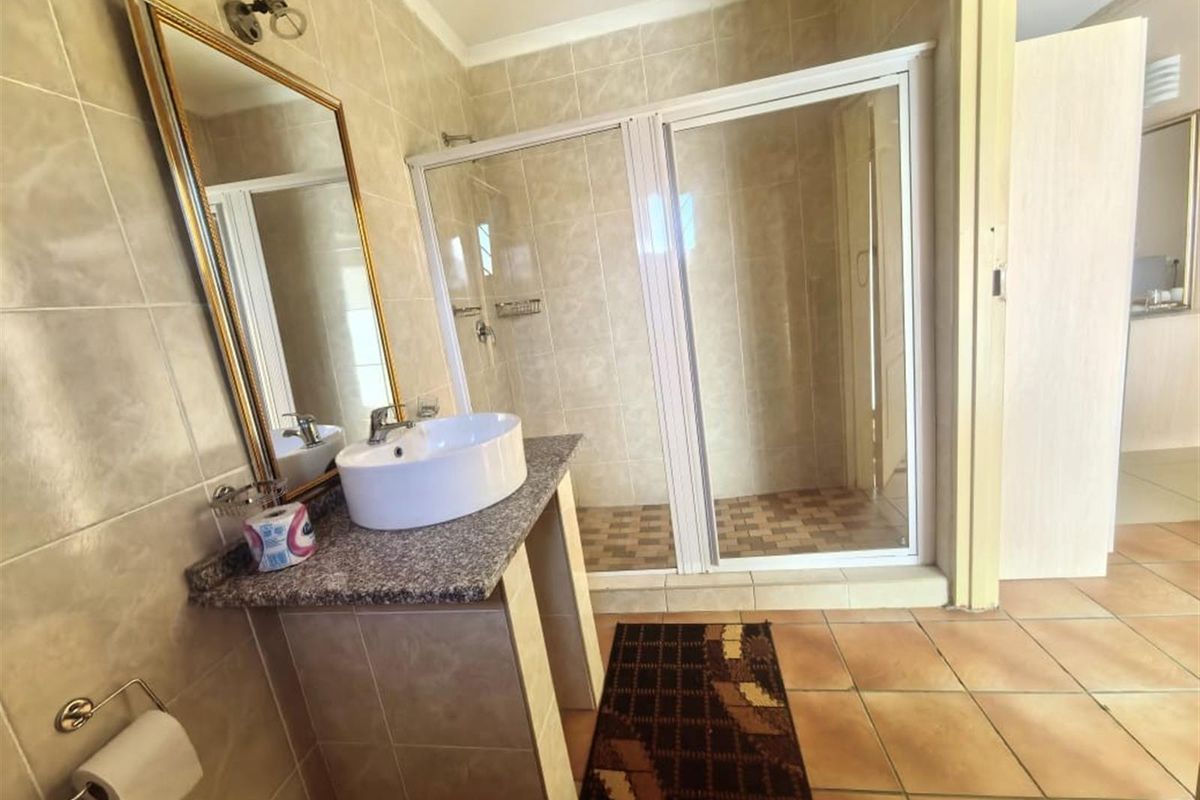 A functional bathroom featuring a walk-in shower with a glass enclosure, a vanity basin set on a granite countertop, and neutral wall tiling.