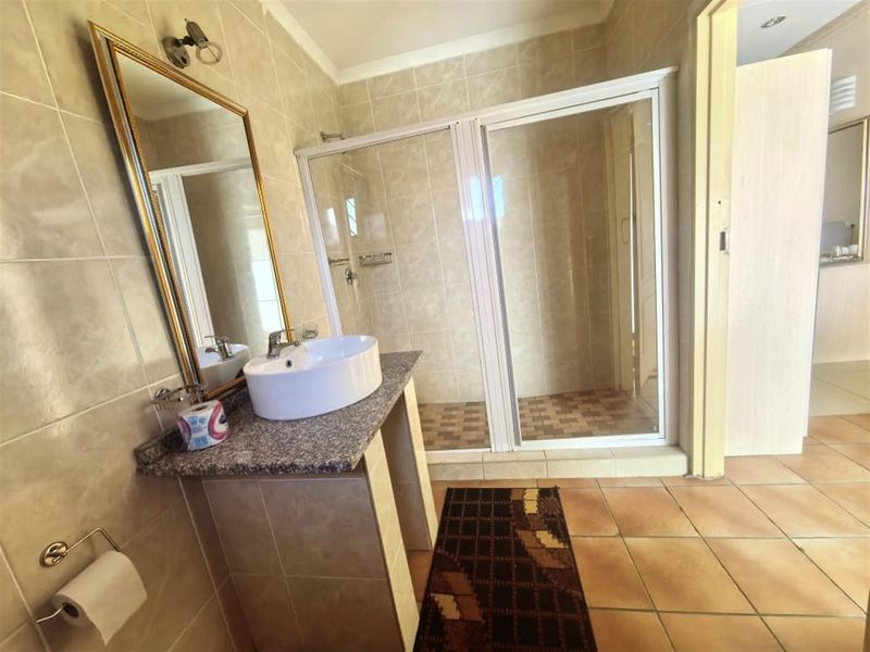 A functional bathroom featuring a walk-in shower with a glass enclosure, a vanity basin set on a granite countertop, and neutral wall tiling.
