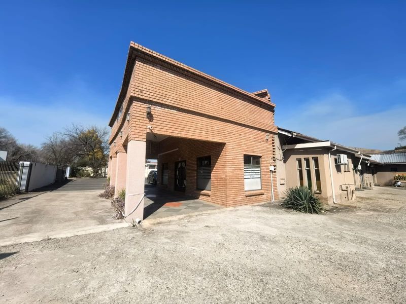 Front exterior view of a brick lodge building featuring a covered entrance, concrete driveway, and security fencing.