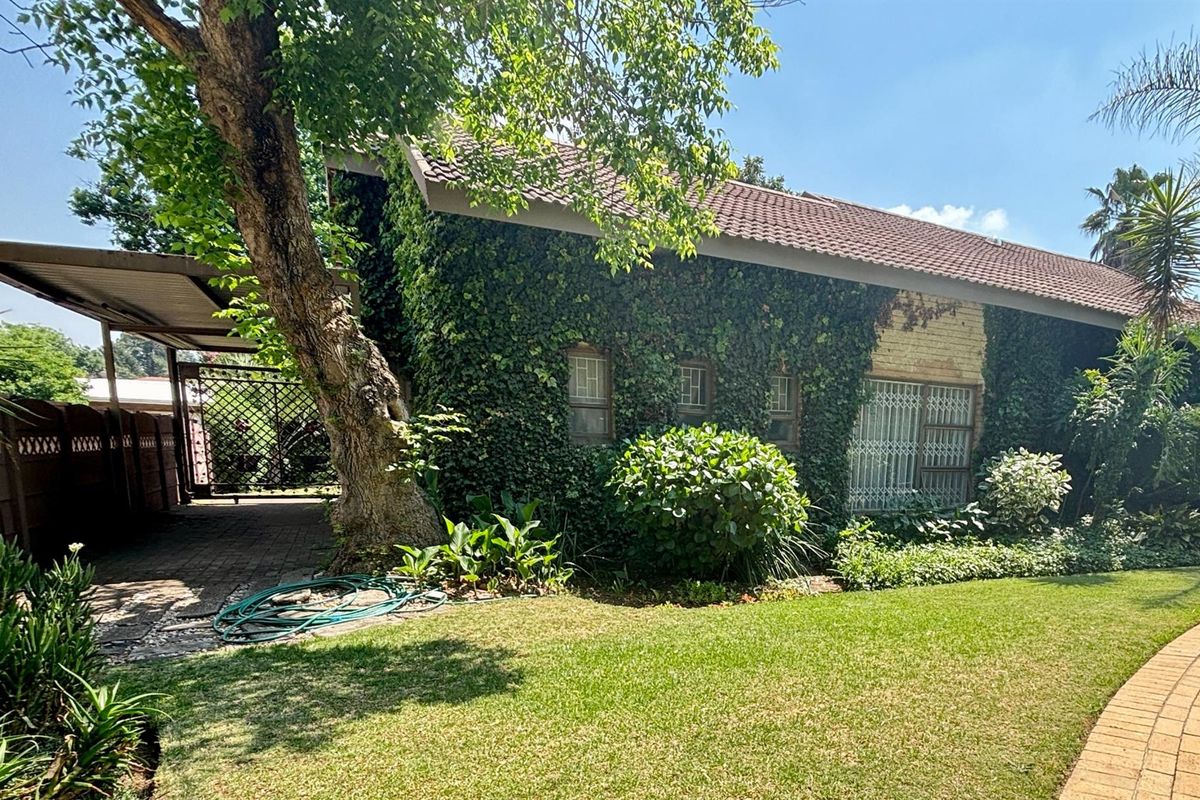 Rear view of the property featuring a tiled roof, brick facade covered in ivy, a paved carport, and a well-maintained garden.