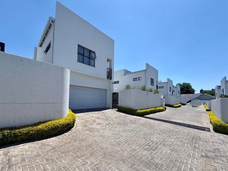 Modern multi-level residential complex featuring paved driveways, automated garage doors, and clean white architectural facades with manicured garden hedges.