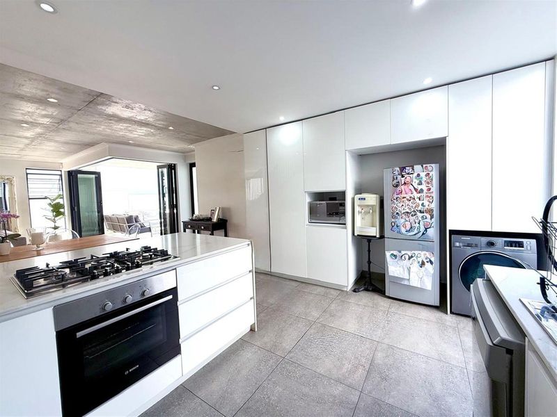 Modern open-plan kitchen featuring a central island with gas hob, sleek white cabinetry, integrated appliances, and seamless flow to the outdoor patio area.
