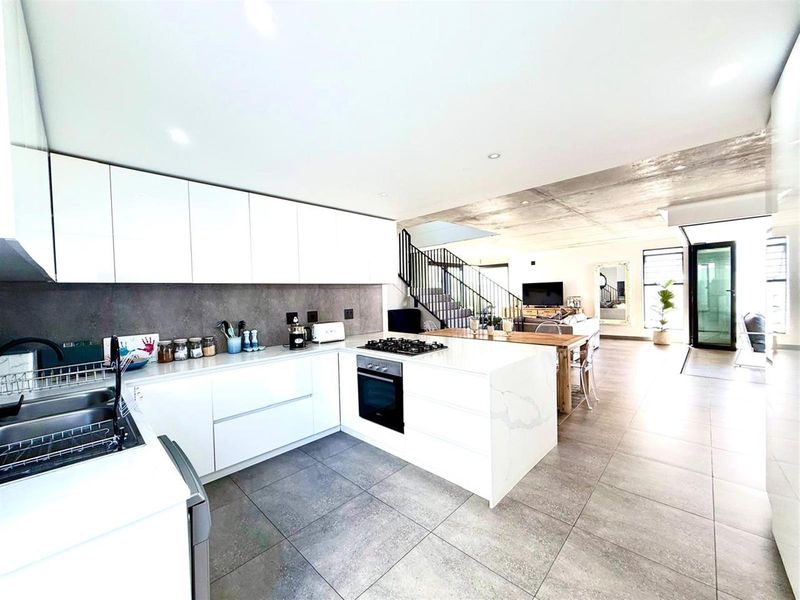 Modern open-plan kitchen featuring sleek white cabinetry, stone countertops, integrated appliances, and a striking exposed concrete ceiling, flowing into the living area.
