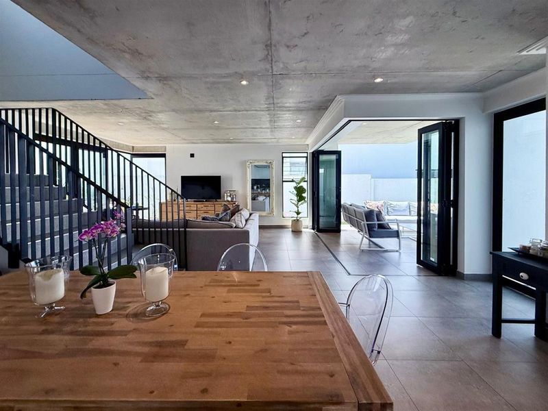 Spacious open-plan living area featuring an exposed concrete ceiling, tiled floors, and seamless indoor-outdoor flow through large bi-fold doors to the patio.