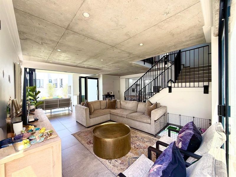 Modern open-plan living area featuring an exposed concrete ceiling, tiled floors, and seamless access to the outdoor patio through large stacking glass doors.