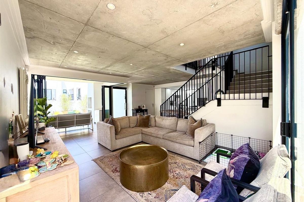 Modern open-plan living area featuring an exposed concrete ceiling, tiled floors, and seamless access to the outdoor patio through large stacking glass doors.