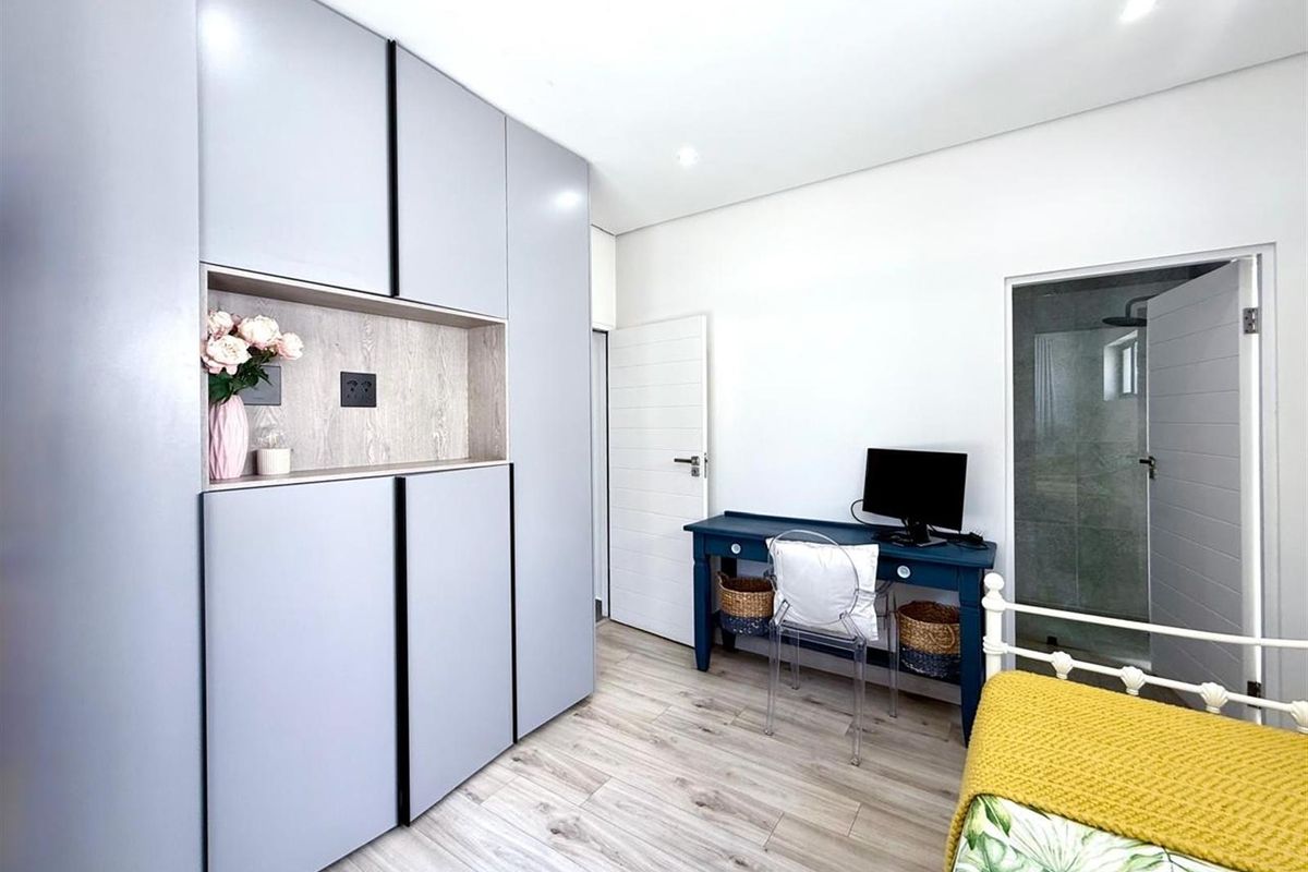 A modern bedroom featuring light-toned laminate flooring, extensive built-in cabinetry with integrated shelving, and direct access to an en-suite bathroom.