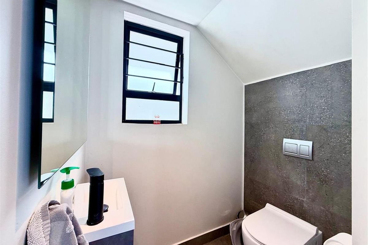 A modern guest bathroom featuring a wall-mounted toilet with a concealed cistern, a vanity basin, and a stylish tiled feature wall.