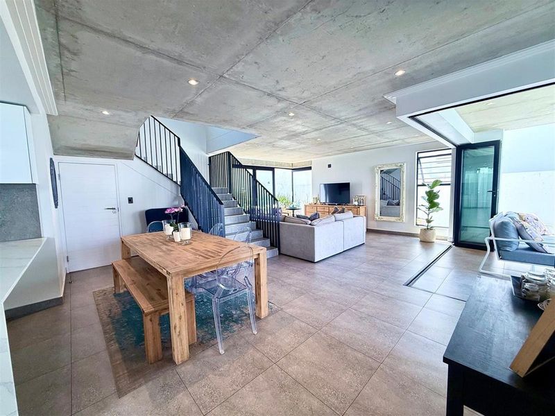 Spacious open-plan living and dining area featuring a modern exposed concrete ceiling, large format floor tiles, and seamless access to outdoor space via sliding doors.