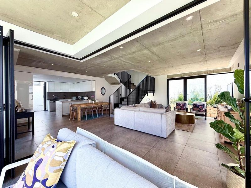 Spacious open-plan living area featuring an exposed concrete ceiling, modern kitchen with island, and seamless flow to the outdoor space via bi-fold doors.