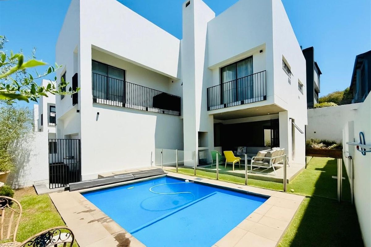 Rear view of a modern two-story home featuring a swimming pool, covered patio with built-in fireplace, and upper-level balconies.