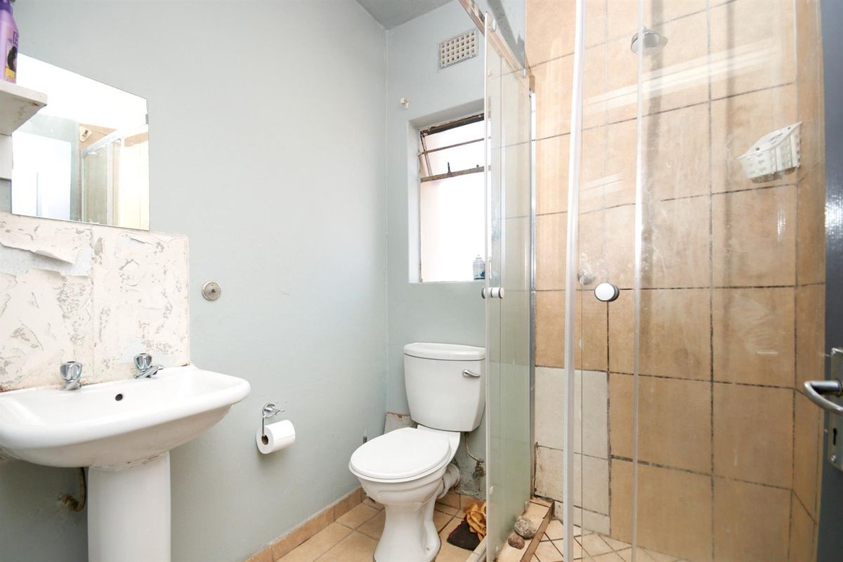 A compact bathroom featuring a pedestal basin, a standard toilet, and a glass-enclosed shower with tiled walls.