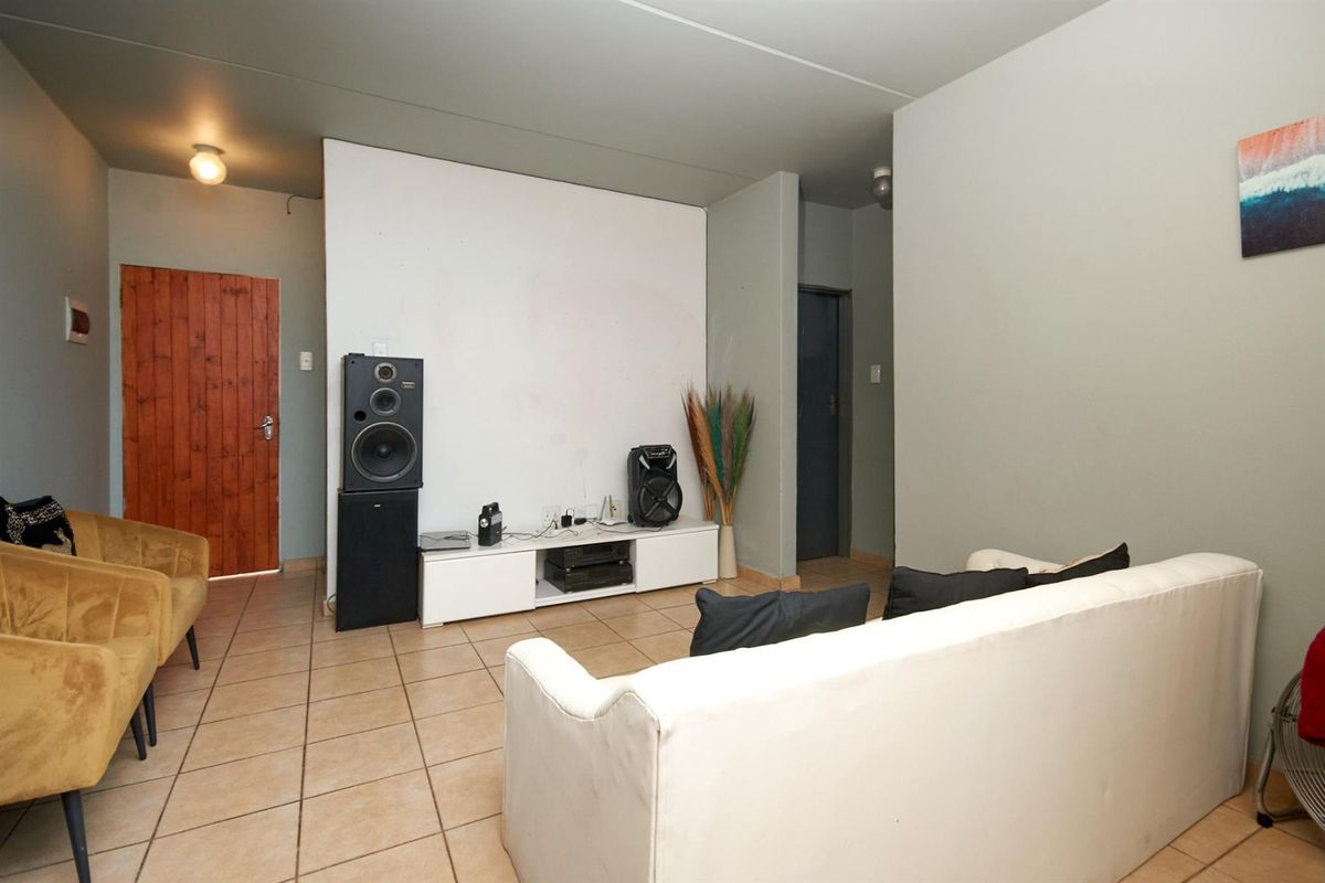 A living room featuring tiled flooring, a central partition wall, and access to adjacent rooms via wooden and standard doors.