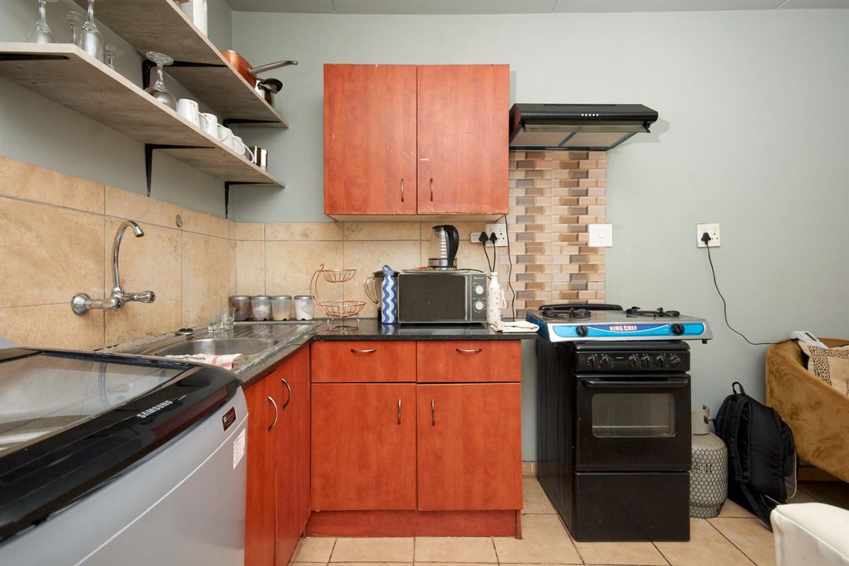 Compact kitchen featuring wooden cabinetry, tiled backsplash, stainless steel sink, and a freestanding stove with an extractor fan.