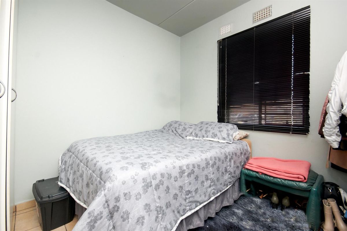 A compact bedroom featuring tiled flooring, a window with fitted venetian blinds, and integrated wall ventilation vents.