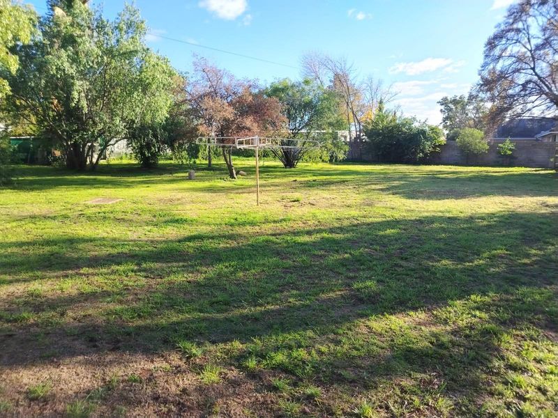 A spacious, open backyard featuring a large lawn area, mature trees, and a fixed rotary clothesline.