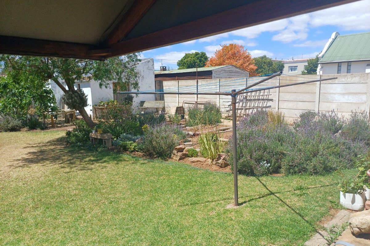 A spacious rear garden featuring a lawn, established garden beds, and a rotary clothesline, enclosed by boundary walls.