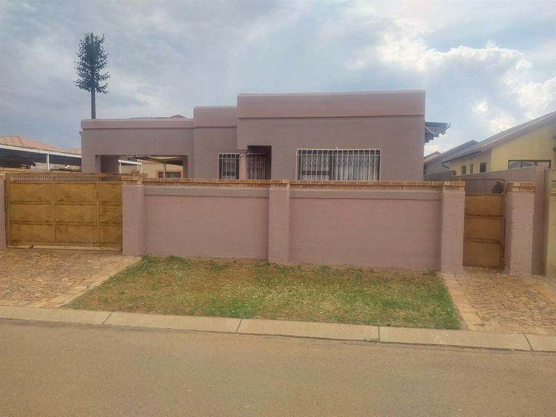 Front view of a single-story house featuring a perimeter wall, security gates, and paved driveway access.
