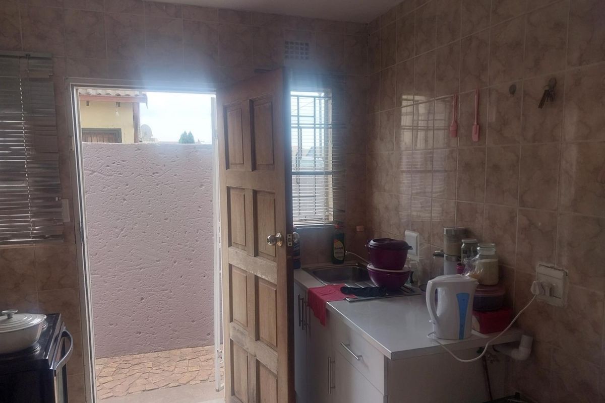 A compact kitchen featuring tiled walls, built-in cabinetry, and a stainless steel sink, with direct access to an outdoor area.