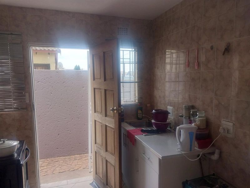 A compact kitchen featuring tiled walls, built-in cabinetry, and a stainless steel sink, with direct access to an outdoor area.