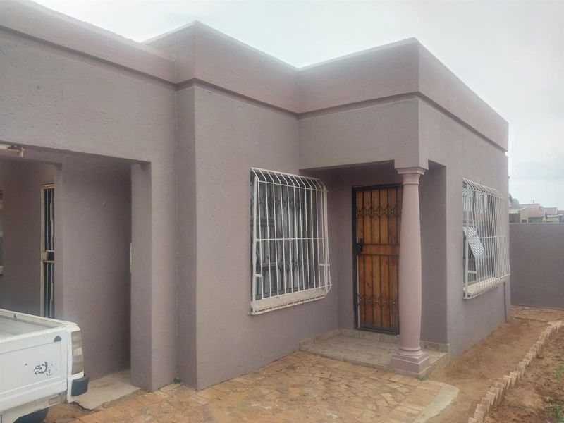 Front exterior view of a single-story residential property featuring a plastered facade, security gates, and a paved entrance area.