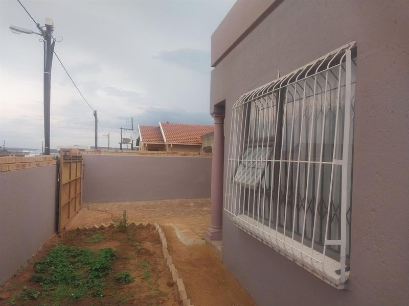 A view of the rear exterior area featuring a paved section, boundary wall, and a window fitted with security bars.
