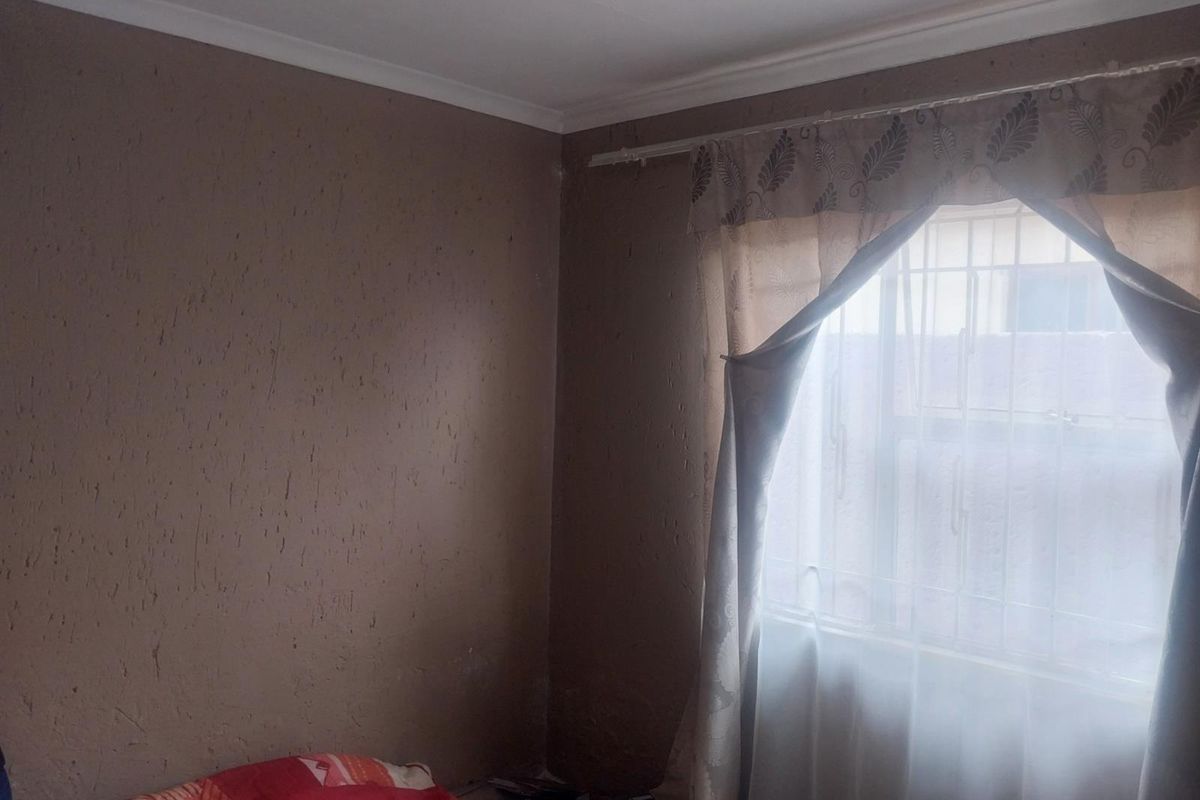 A bedroom featuring textured walls, coving, and a window fitted with security bars.