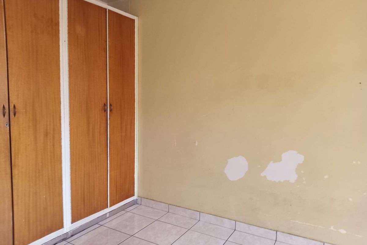 A bedroom featuring built-in wooden cupboards and tiled flooring, currently vacant and requiring minor cosmetic wall repairs.