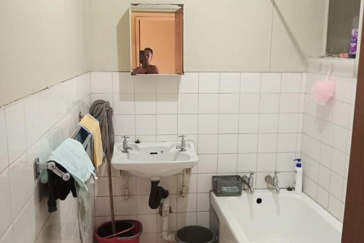A compact bathroom featuring a standard bathtub, wall-mounted basin, and tiled walls, requiring cosmetic updates to improve its overall condition and aesthetic appeal.