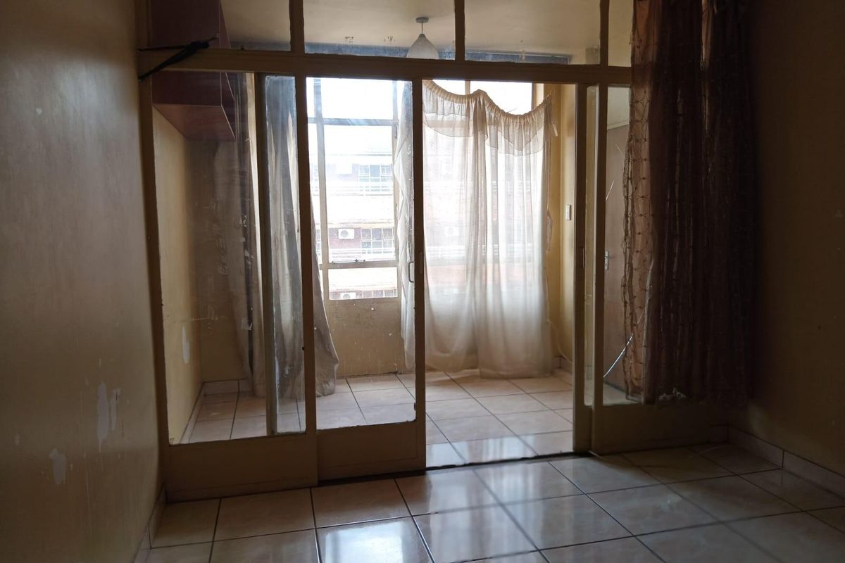 A living area featuring tiled flooring and a large glass partition leading to an enclosed balcony space.