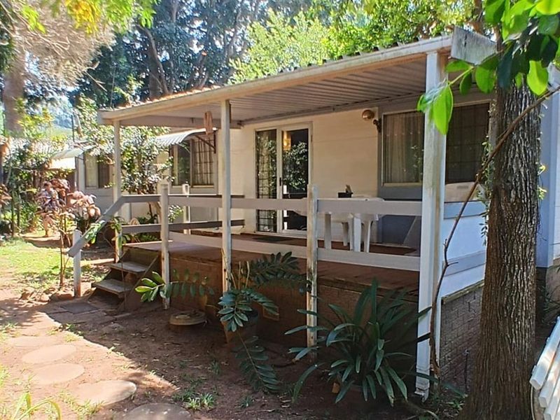 A rear view of a retirement unit featuring a covered timber deck, sliding glass doors, and a surrounding garden setting.