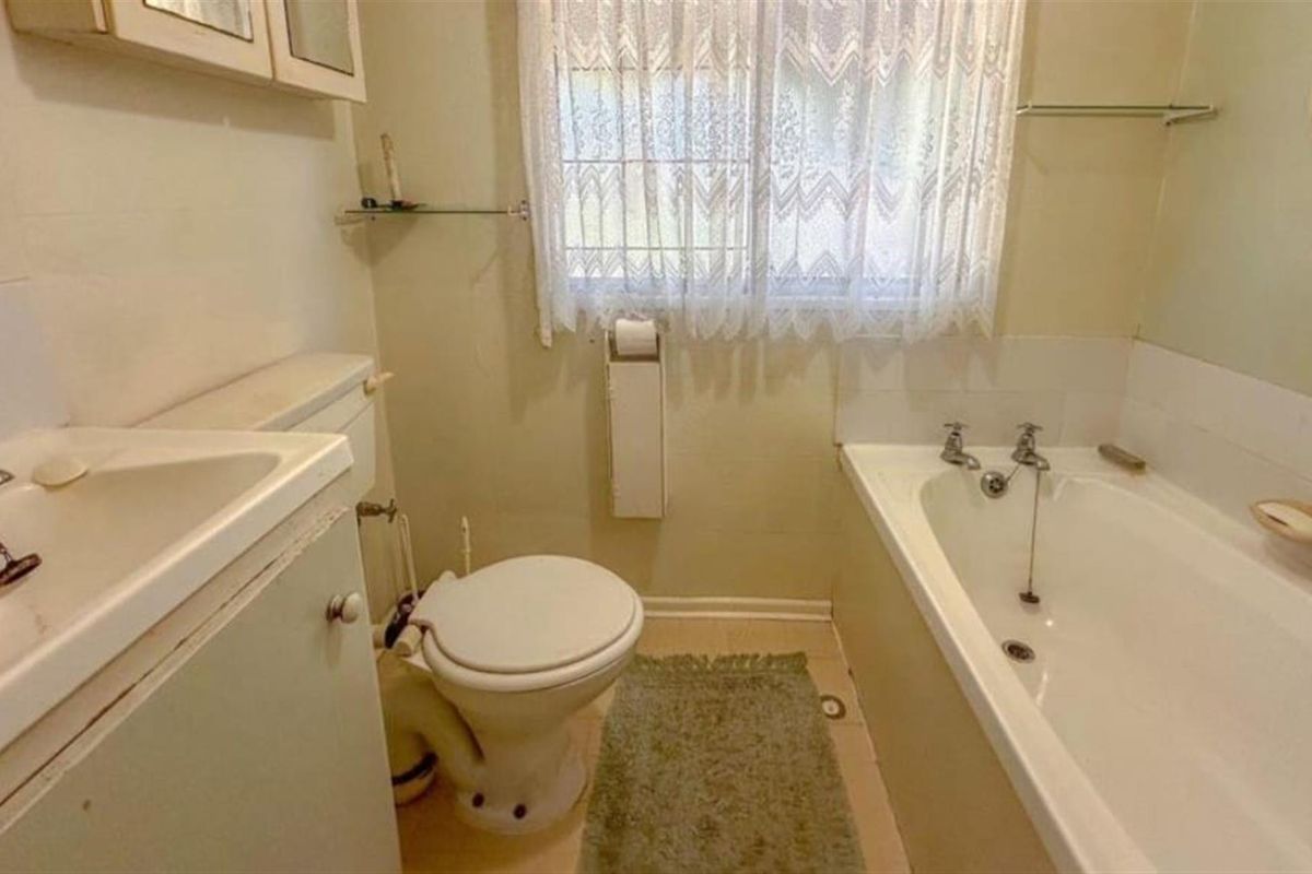 A dated bathroom featuring a standard bathtub, toilet, and vanity unit, offering potential for modernization and cosmetic updates.