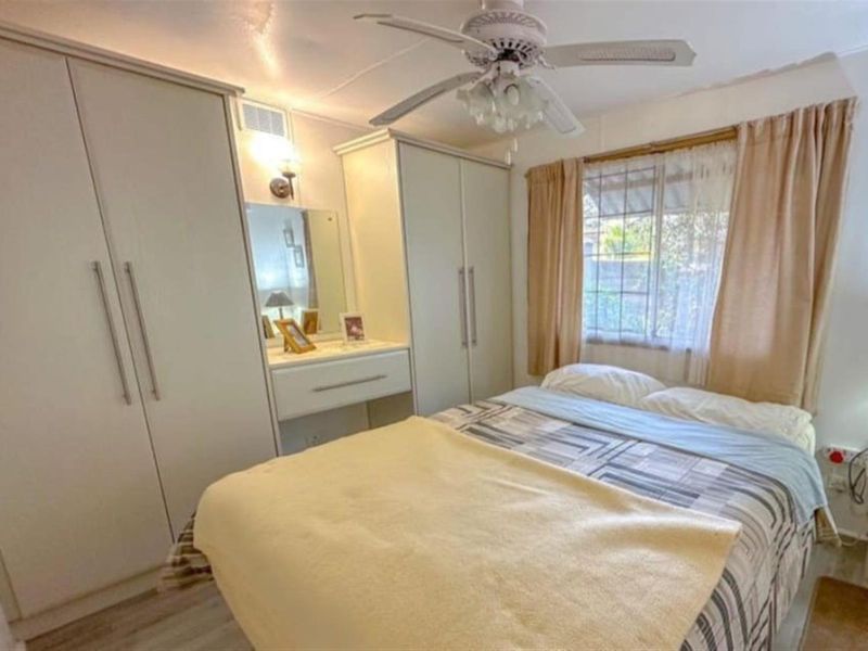 A functional bedroom featuring built-in wardrobes with an integrated vanity unit, ceiling fan, and neutral laminate flooring.