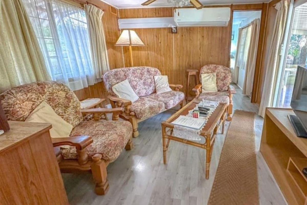 A living room featuring wood paneling, a ceiling fan, and a split system air conditioner, finished with modern laminate flooring.