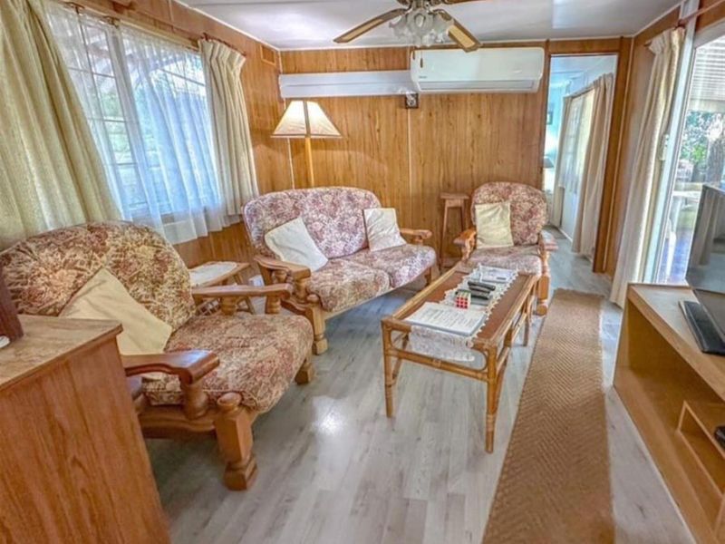 A living room featuring wood paneling, a ceiling fan, and a split system air conditioner, finished with modern laminate flooring.