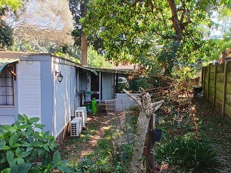 Rear exterior view of the property featuring a precast boundary wall, established garden area, and external air conditioning units.