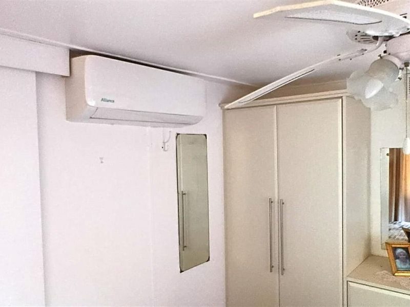 A bedroom featuring a built-in wardrobe, ceiling fan, and wall-mounted air conditioning unit.