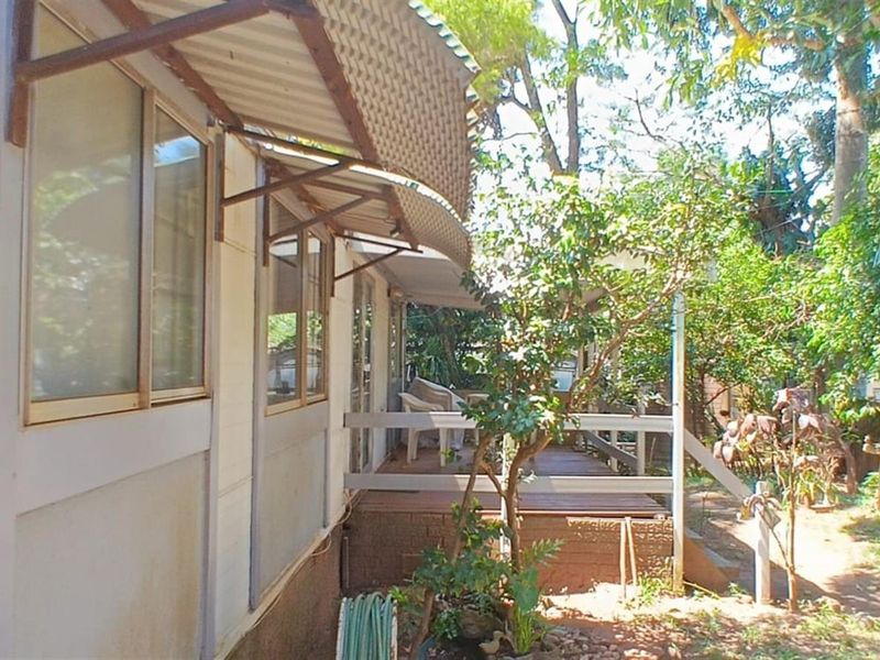 Rear exterior view of the property featuring a timber deck, corrugated metal awning, and established garden surroundings.