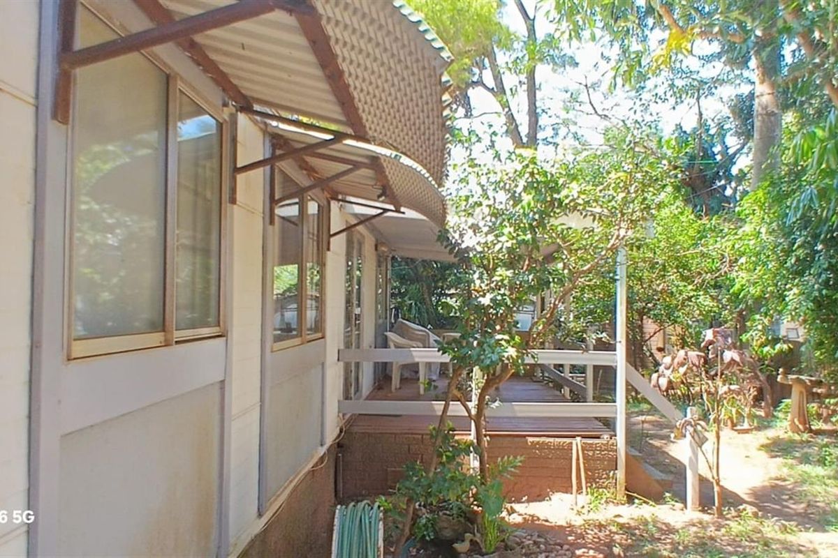 Rear exterior view of the property featuring a timber deck, corrugated metal awning, and established garden surroundings.