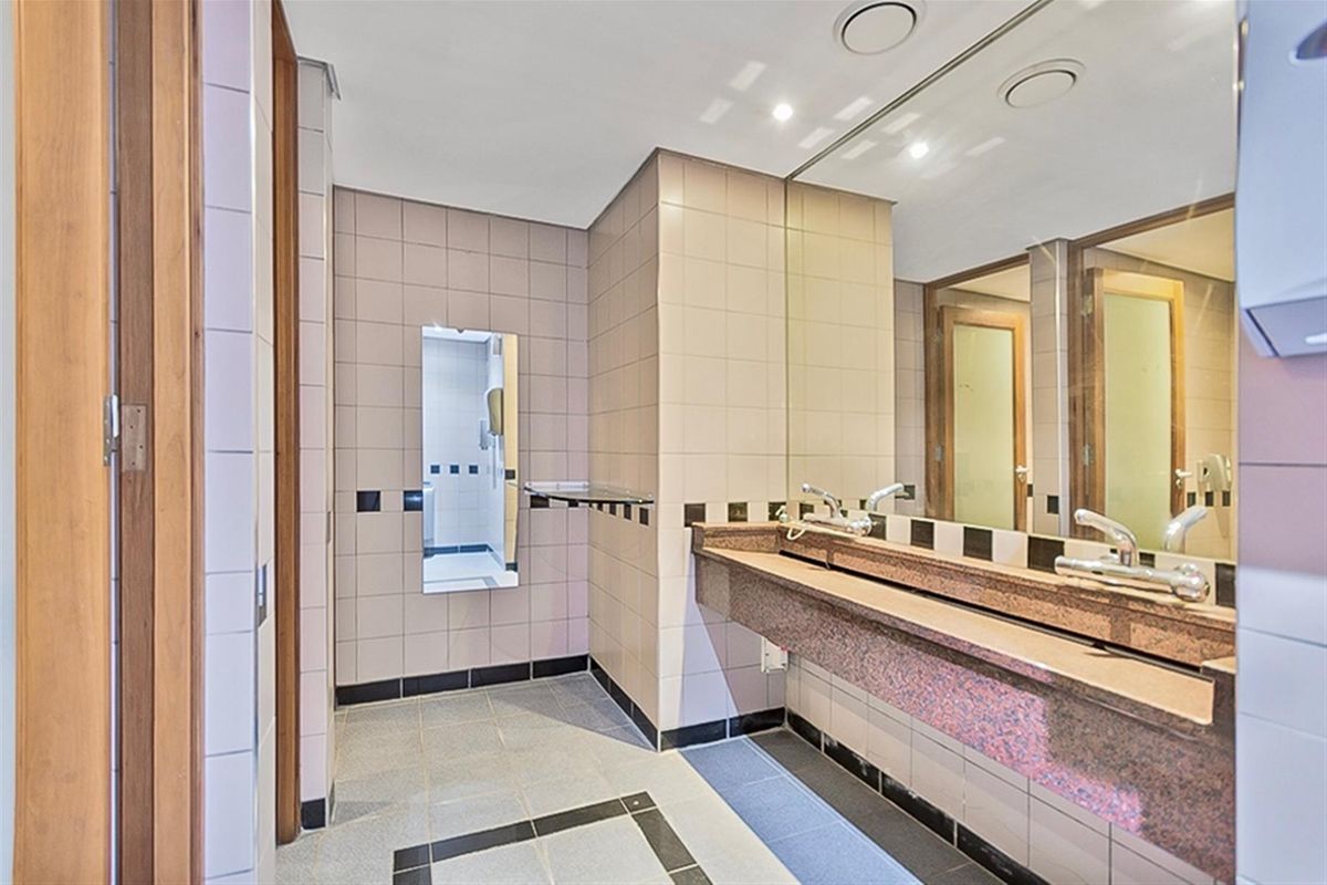 Commercial restroom featuring a granite vanity countertop, large wall-mounted mirror, and tiled wall and floor finishes.