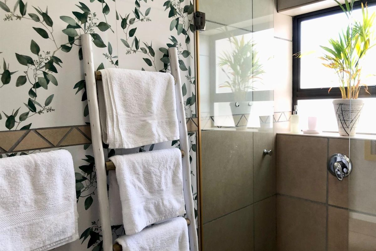 A modern bathroom featuring a glass-enclosed shower, decorative botanical-patterned wall tiles, and neutral floor-to-ceiling tiling.