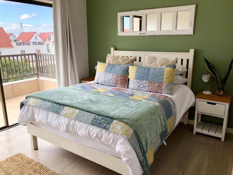 A bright bedroom featuring wood-look flooring, a feature wall, and direct access to a private balcony with outdoor views.