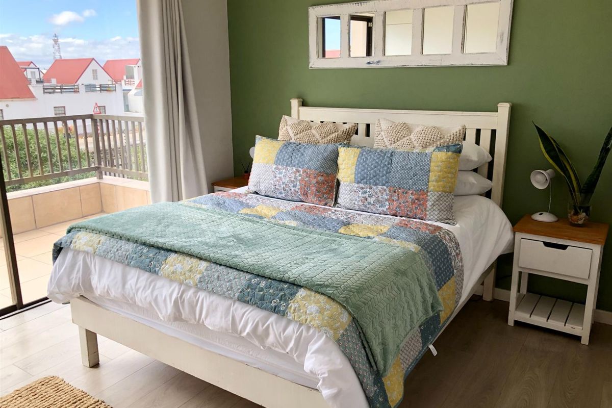 A bright bedroom featuring wood-look flooring, a feature wall, and direct access to a private balcony with outdoor views.