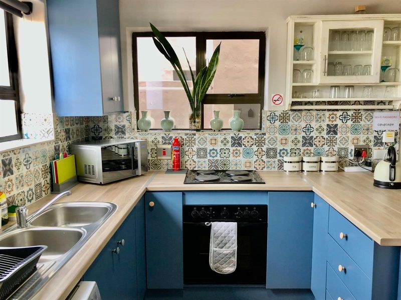 A compact kitchen featuring blue cabinetry, wood-look countertops, patterned tile splashbacks, a built-in oven, and a stainless steel double sink.