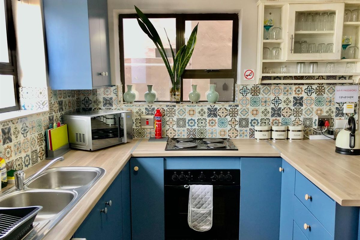 A compact kitchen featuring blue cabinetry, wood-look countertops, patterned tile splashbacks, a built-in oven, and a stainless steel double sink.