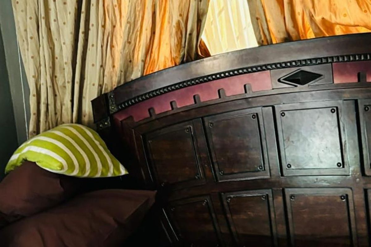 A bedroom featuring a dark wood headboard and window curtains.