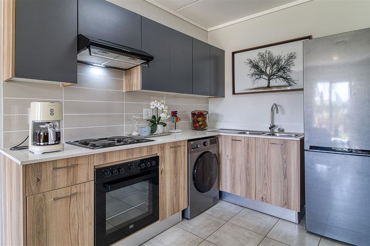 Modern kitchen featuring wood-grain cabinetry, sleek dark overhead cupboards, integrated gas hob, built-in oven, extractor fan, and tiled flooring.